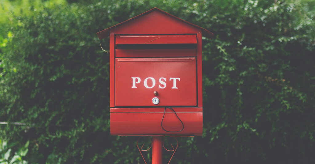Ein roter Briefkasten steht vor einer Hecke