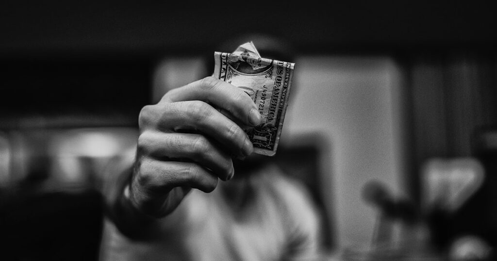 Ein Mann hält einen Geldschein hin und verdeckt damit sein Gesicht