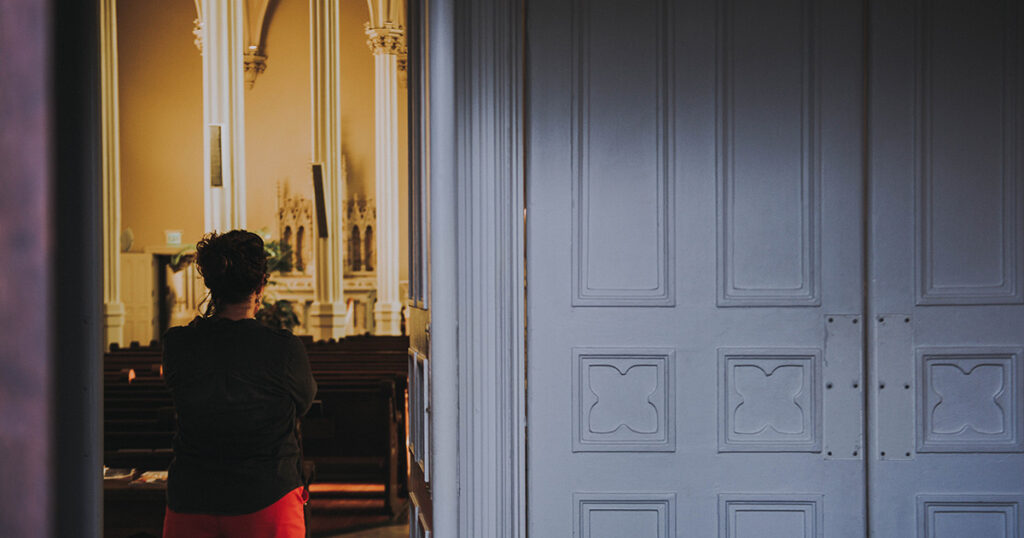Eine Frau steht an einer Kirchentür und schaut in den Kirchenraum.