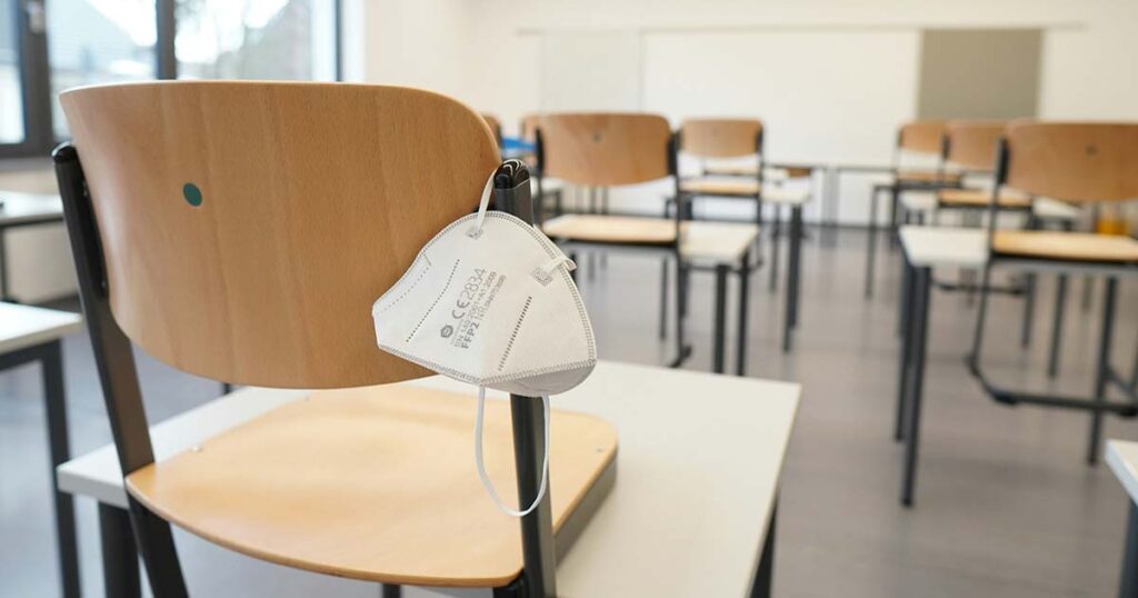 Eine FFP2-Schutzmaske hängt in einem Klassenzimmer an einem Stuhl